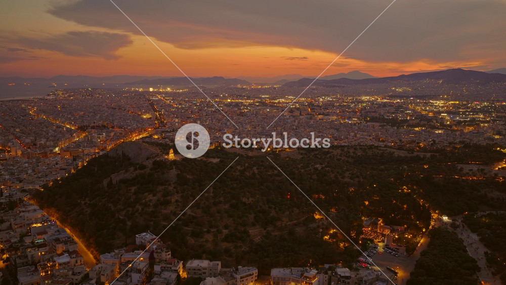 Sweeping aerial view of athens, greece, during twilight, showcasing the sprawling city's illuminated street grid, the dark silhouette of lycabettus hill, and the aegean sea on the horizon