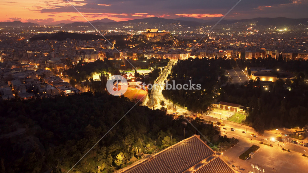 Majestic aerial view of the illuminated Panathenaic stadium, also known as kallimarmaro, nestled in the sprawling cityscape of Athens, Greece, during the enchanting twilight hour.
