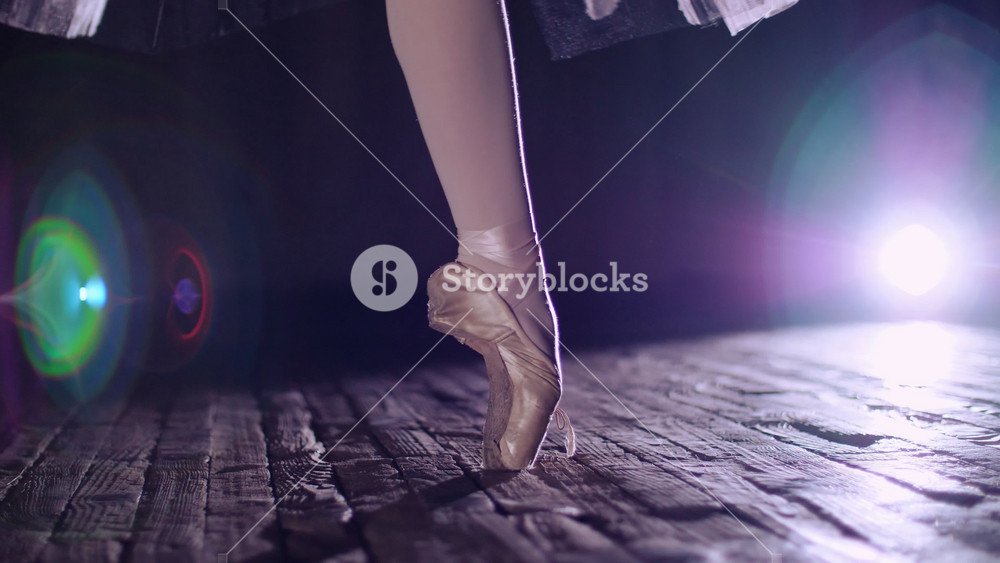 Close up of ballerina rotating on pointe shoes in spotlight on theater boards. Atmospheric moment of classical ballet.