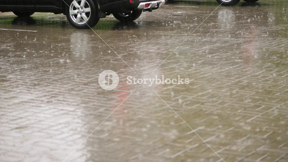 Heavy rain floods city parking lot with water splashing around cars. Torrential downpour creating large puddles on asphalt.