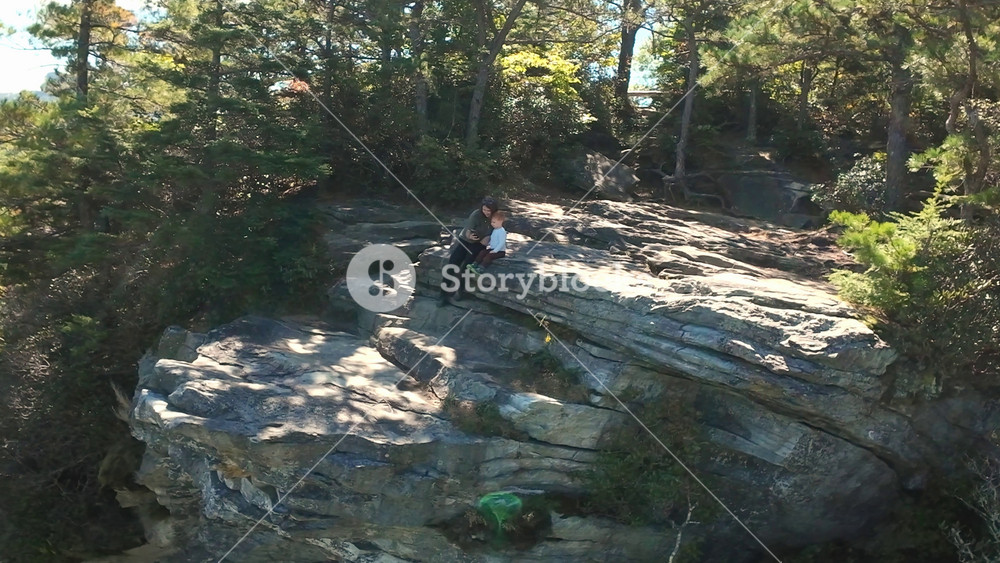 Group Relaxing Atop Scenic Mountain Edge. Aerial Shot Of People On Rocky Hillside Enjoying Nature. Vast Panoramic View From Above Of Friends