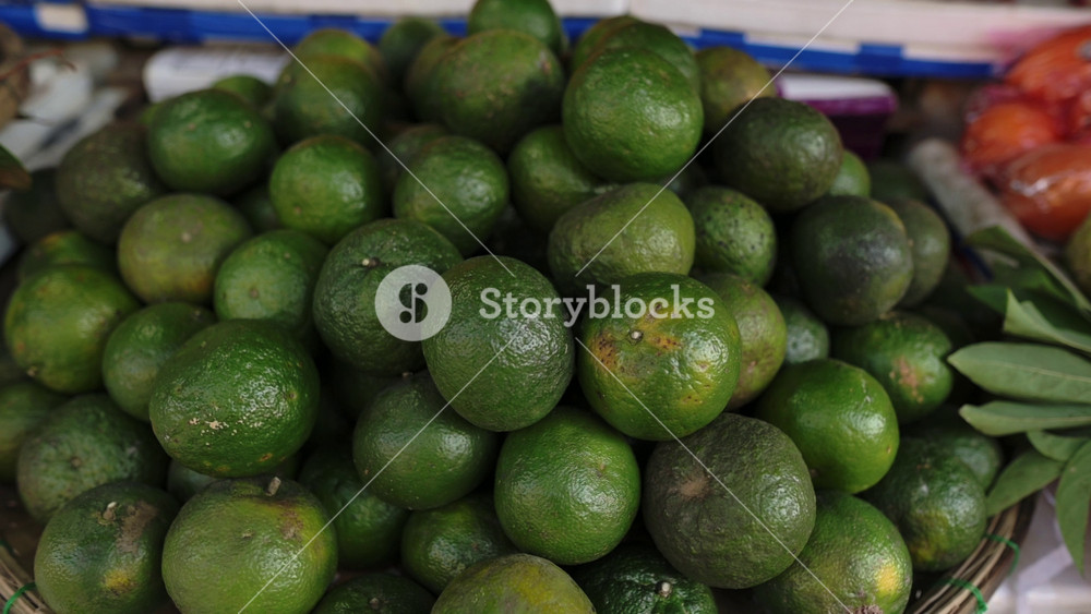 Colorful Display Of Limes And Foliage. Brightly Arranged Citrus Fruits With Textured Leaves On Market Stall. Closeup Of Vibrant Citrus