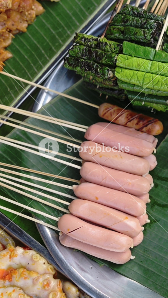 Vertical screen Skewered Sausages On Banana Leaf, Vietnam Street Market Display Showing Raw Pink Sausages Stacked On Wooden Skewers Beside