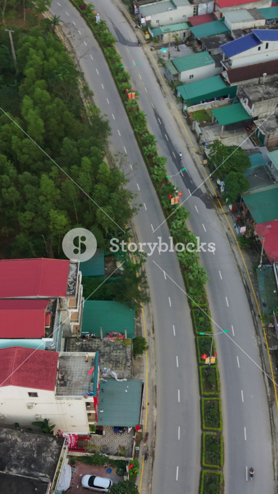 Vertical screen Aerial View of Curved Village Road, Winding Asphalt Lanes With Planted Median along Colorful Rooftops, Phong Nha, Vietnam.
