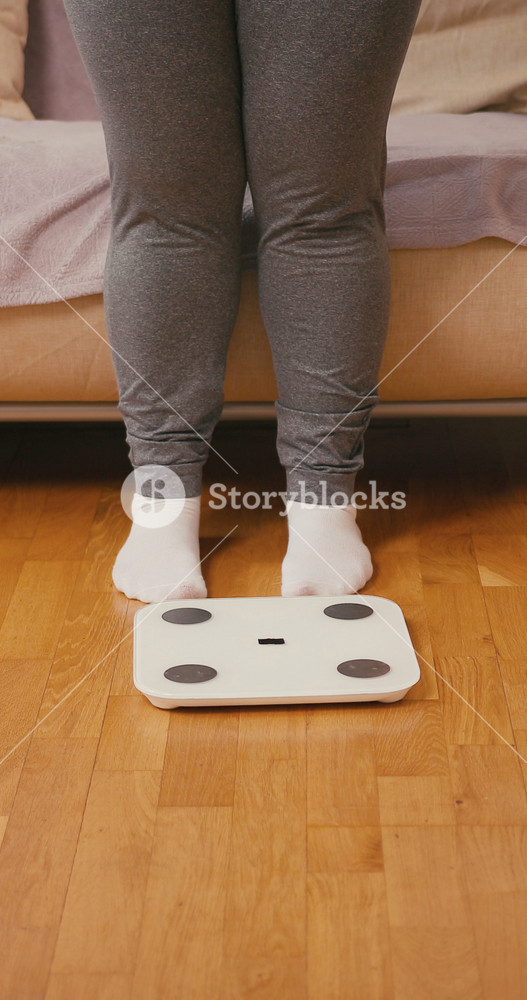 Female legs step onto white electronic scales. Adult woman positions feet firmly on surface to check current body weight during home