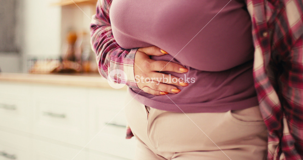 Sick Ill Overweight Woman Suffering from Period Cramps, Painful Stomach Ache at Kitchen. Girl holding Belly, Feeling Abdominal Menstrual