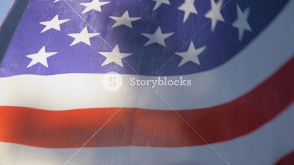 The American flag waves proudly in the radiant sunlight against the clear blue sky. Its vibrant colours embody the ideals of freedom