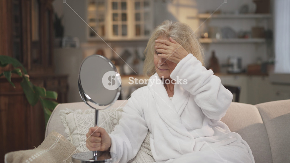 Stay beautiful in old age, portrait of pretty elderly lady with mirror in room. Natural female beauty, mature woman looking on her face and