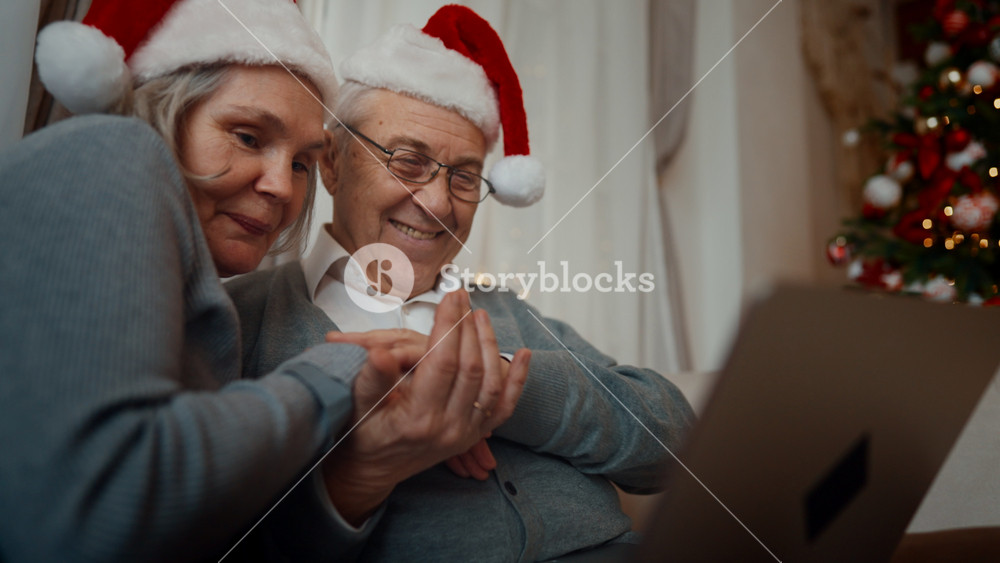 Portrait of joyful aged woman and man congratulating friends in Christmas online. Pretty grey-haired lady and her husband in funny Santa