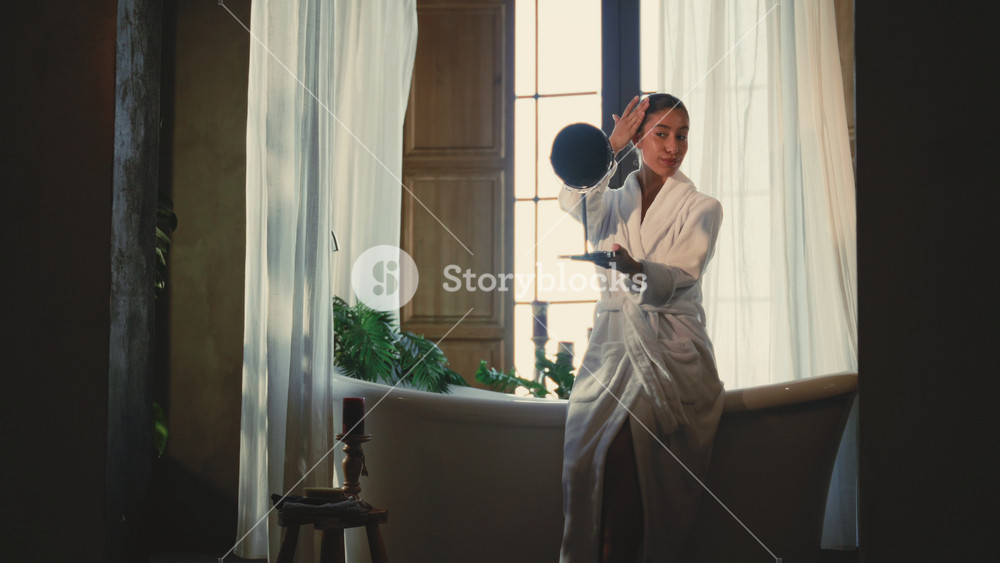 Charming Arabic adult woman relaxing in bathroom in morning, looking at mirror. Daily beauty treatments at home for stay beautiful and young
