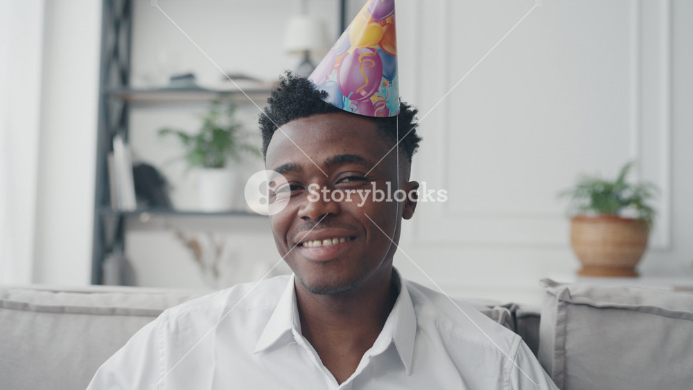 Happy african american man in Birthday cap smiling to camera, portrait at home. Celebrating anniversary or coming of age, young guy become