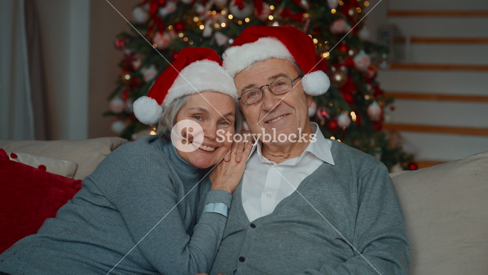 Portrait of happy elderly spouses at home in Christmas holidays, smiling people. Joyful married couple with funny Santa hats, grandmother