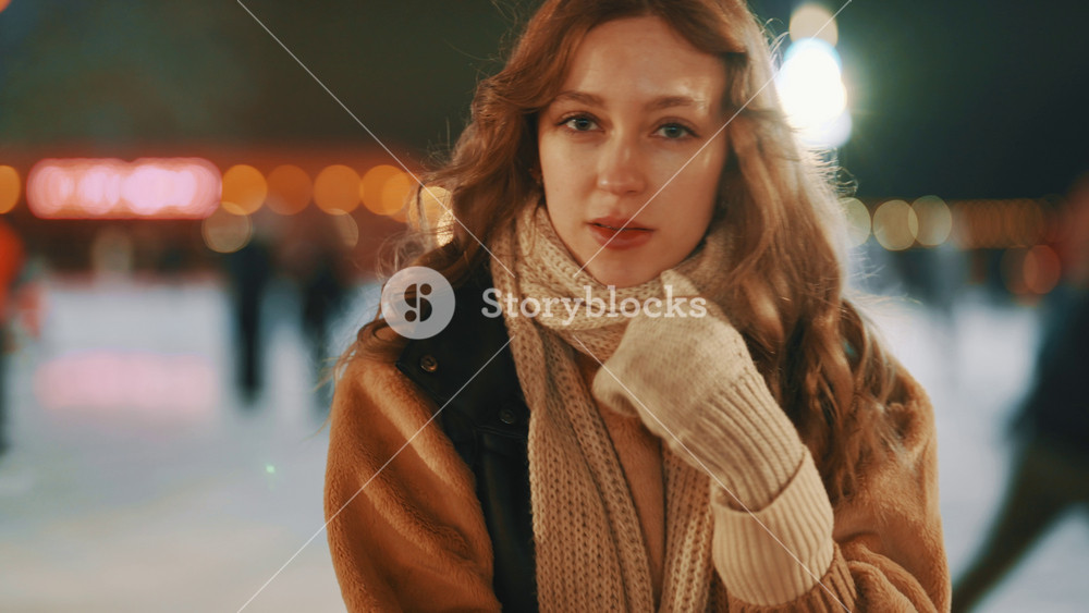 Portrait of teenager girl outdoors in city in winter night, lady feeling cold. Charming young woman with long red hair standing alone on ice