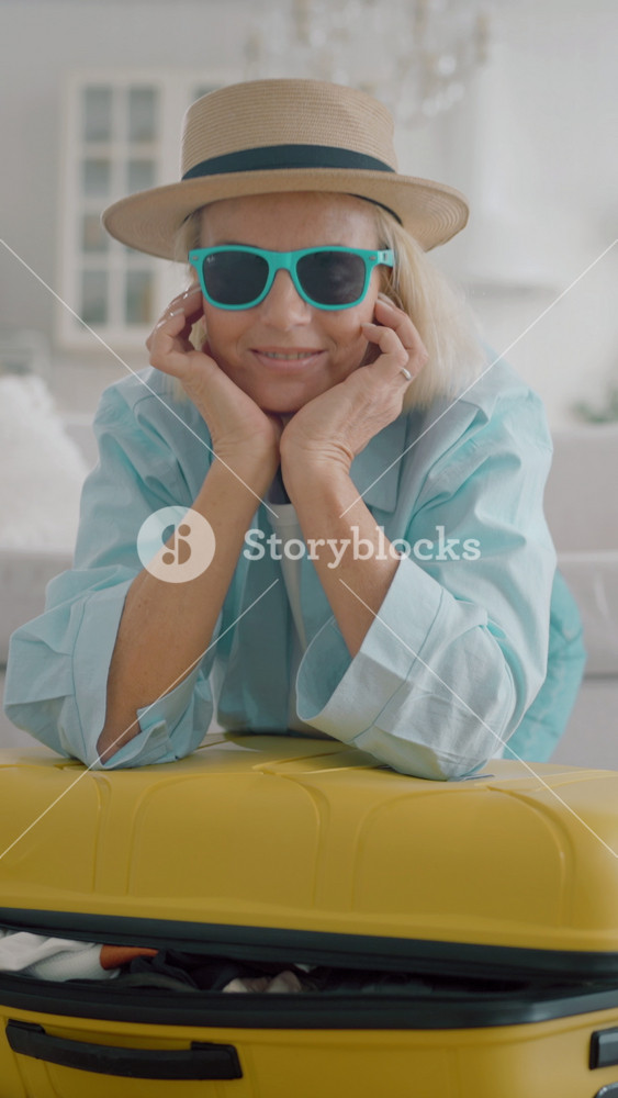 Portrait of stylish senior lady traveler leaning on her suitcase in living room. Smiling female person enjoying future weekend trip, looking