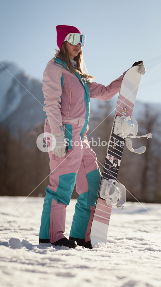 Sport and recreation in ski resort in mountains, beautiful woman in overall posing with snowboard on snow. People enjoying skiing and
