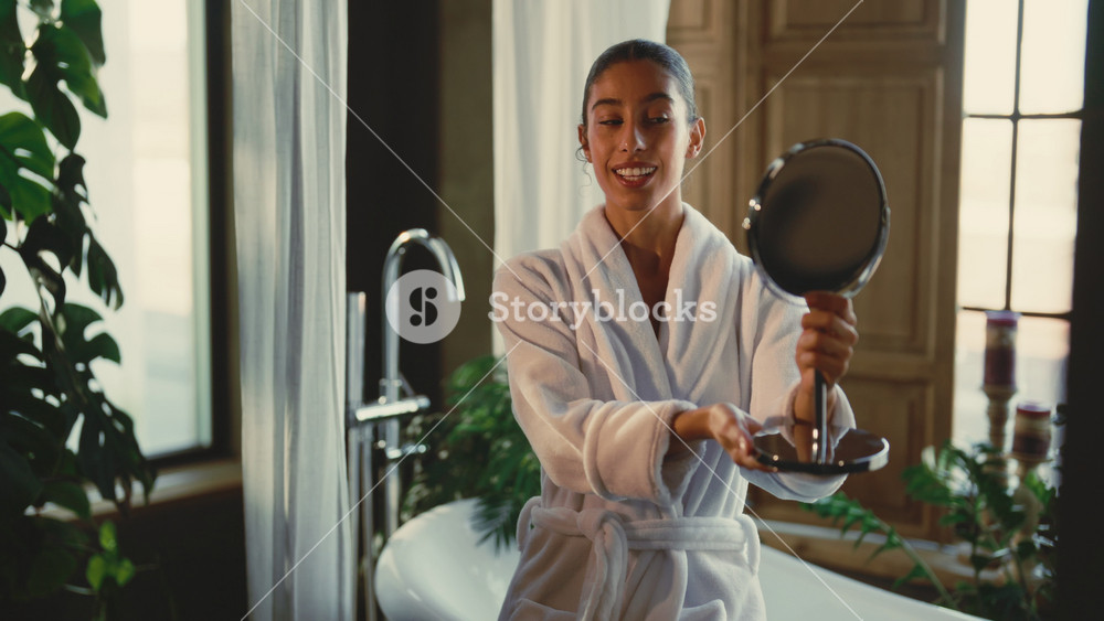 Daily morning routine, woman admiring her beautiful skin after treatments. Portrait of happy Arab lady admiring her face in small mirror in