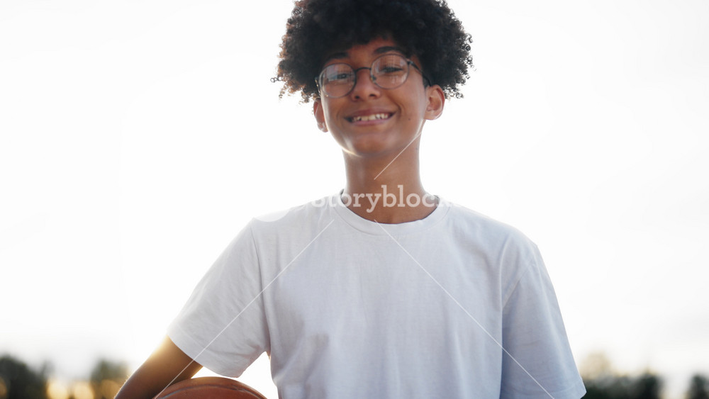 Future champion of basketball, adolescent black boy with ball in hands smiling. Cute teenager with black curly hair and glasses looking at