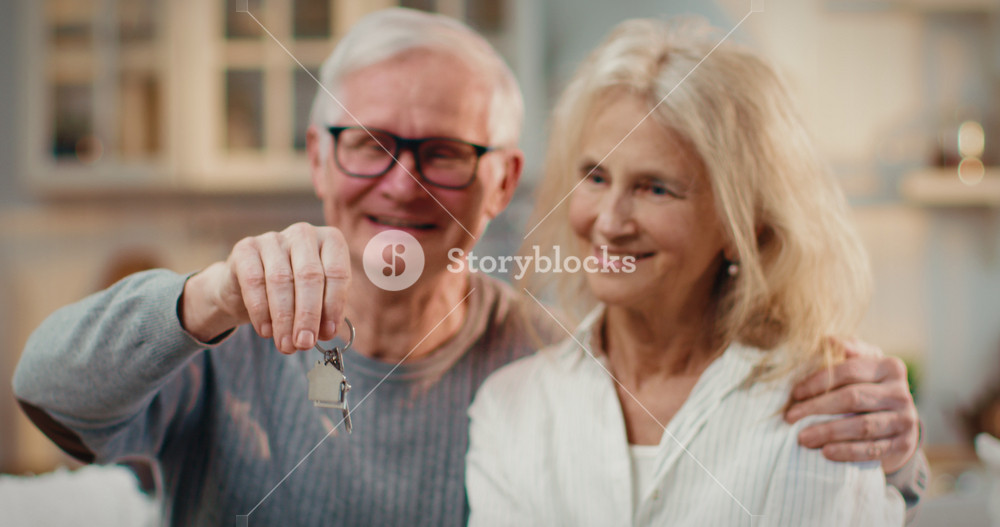 Happy elderly spouses holding keys of new apartment or house, finish of mortgage . Old married couple rejoicing of buying own home