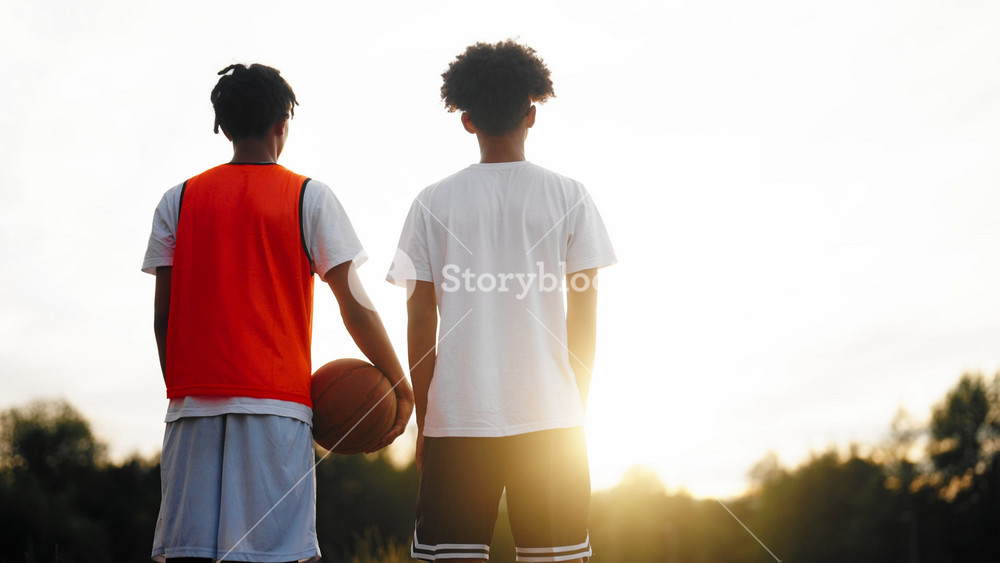 Two friends after basketball match, back view, teenagers boys admiring nature. Streetballers resting after hard workout outdoors, young