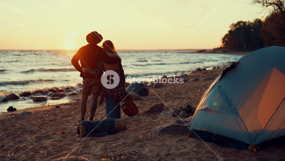 Camping on happy lovers embracing in sunset or sunrise, back view. Love and tenderness, traveler admiring beautiful seascape in morning or
