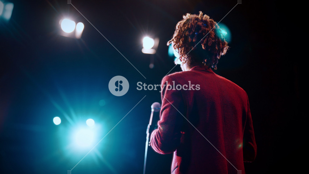 Motivational speech of popular life coach, back view of male speaker on stage. Silhouette of stylish male person with dreadlocks performing