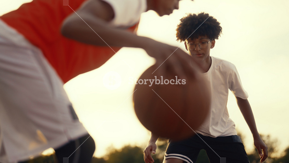 Juniors sportsmen practicing basketball, teen viewing ball in hands of opponent. African american boy playing with friends or brothers in