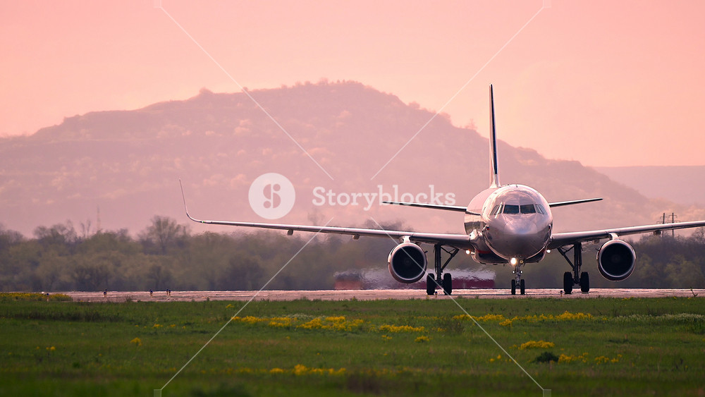 Huge airplane jet maneuvering after landing at international airport landing zone at beautiful sunset clouds sky and big mountings. 4k super