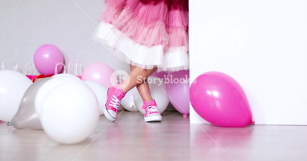 Joyful little girl in pink dress and sneakers stand with big present gift box, balloons at home birthday party streamers, Happy birthday. Celebrating