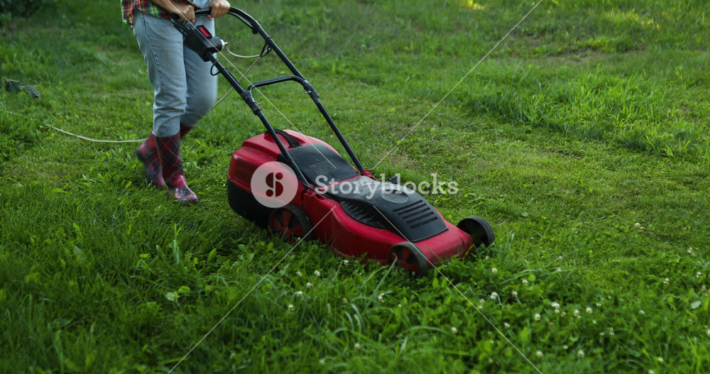 Woman mows the lawn with a lawn mower grass at home garden, gardener woman working, Beautiful summer landscape, sunlight, great design for any purposes, gardening concept