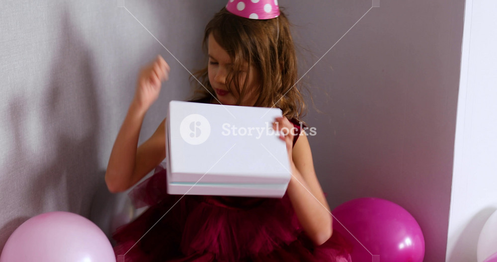 Little girl opening presents at her birthday party, curious child peeking into the Birthday gifts that she already received.