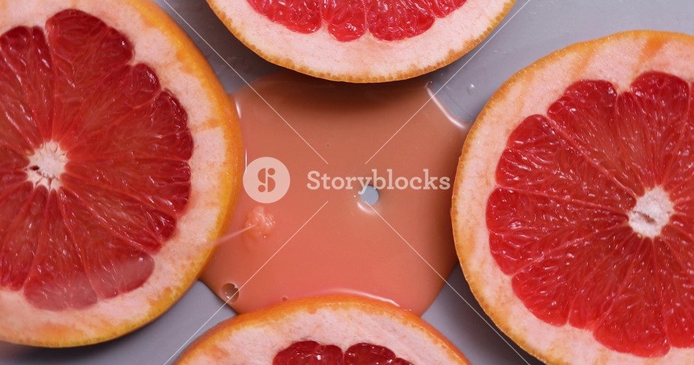 Top view rotation of fresh slice of grapefruits juice and gel serum pours, organic cosmetics, vitamin C, fresh citrus fruits, grapefruit extract
