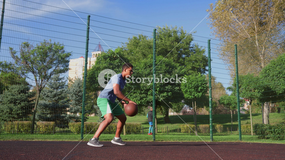Motivated athletic African American male basketball player jumping in the air, performing powerful slam dunk with one hand during sports training on outdoor court.