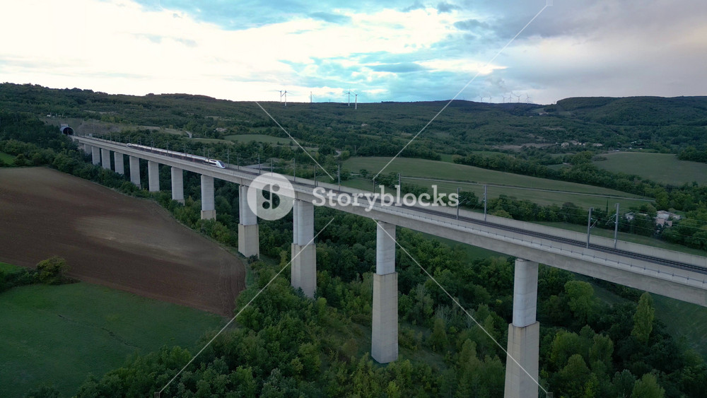 Passenger train crossing the railway flyover and entering the tunnel near La Roche-Sur-Grane (Drome - France). Overlooking the wind farm on the hill