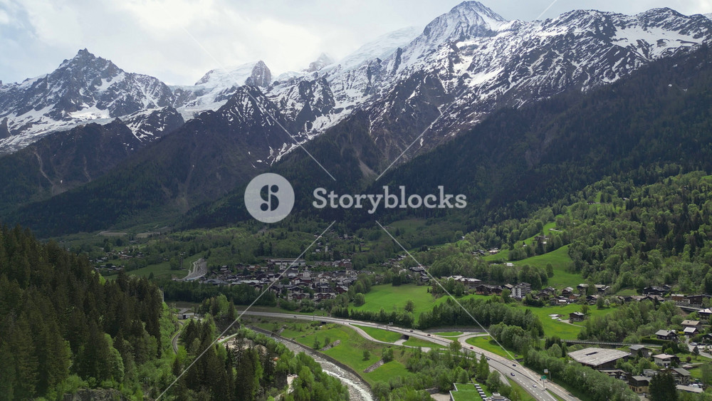 Aerial drone view of the scenic road entering the Chamonix valley, surrounded by alpine forest, village houses and snow covered Mont Blanc mountains in the French Alps.