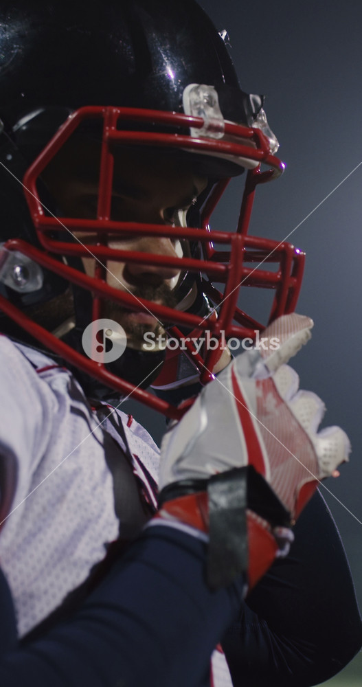 Cinematic vertical slow motion close-up of an American football player in full gear, wearing a black helmet and red facemask, captured
