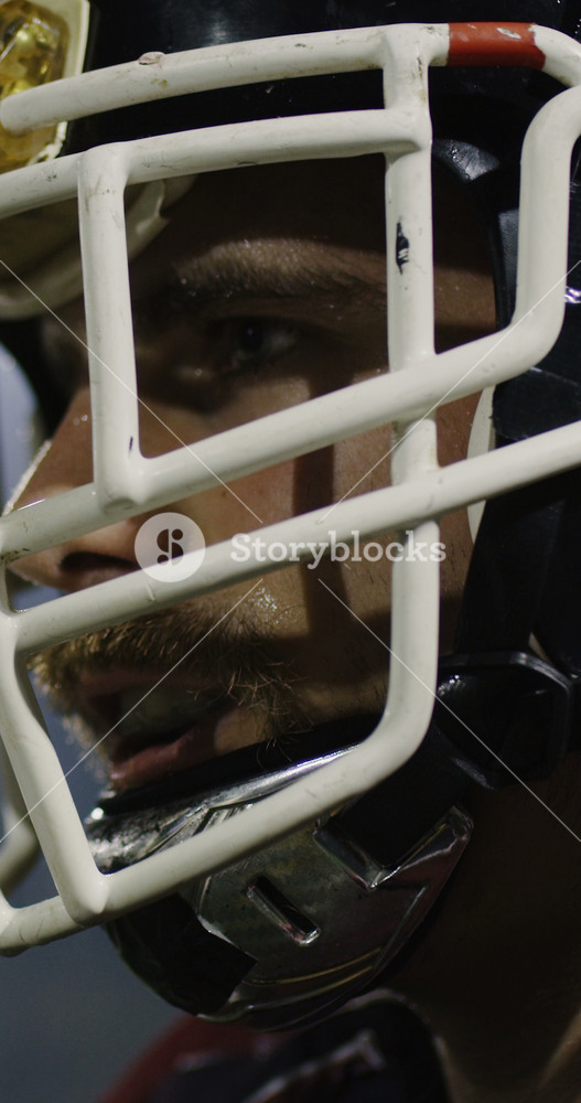 Cinematic vertical slow motion close-up of an American football player in full gear, wearing a black helmet and red facemask, captured