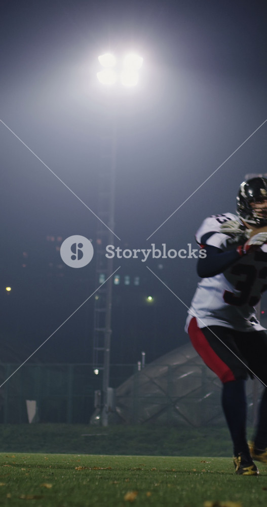 Close-up of American football player in red jersey catching the ball under bright stadium lights at night, intense sports action and