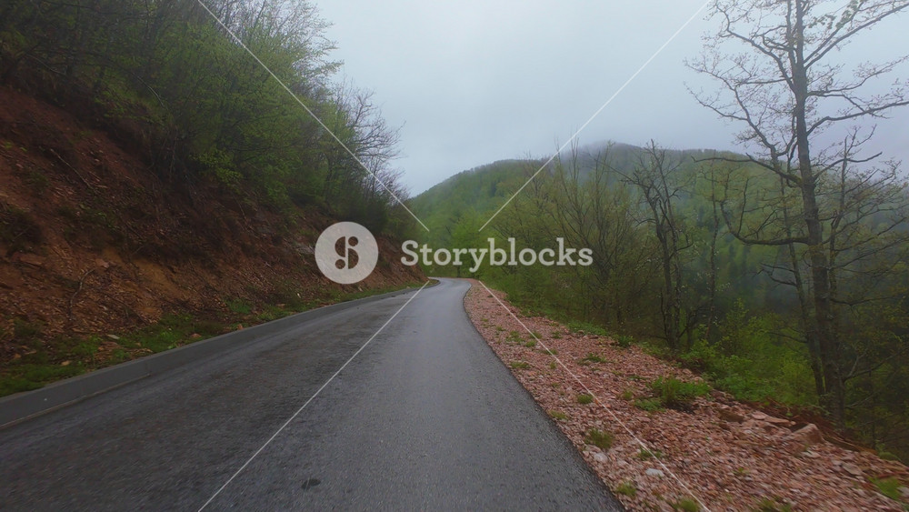 Aerial view of a foggy mountain road weaving through verdant hills, misty forests, and scenic valleys, offering a breathtaking natural