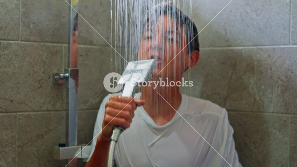 A cheerful teenage boy is having fun in the shower, singing his favorite song into the shower instead of a microphone