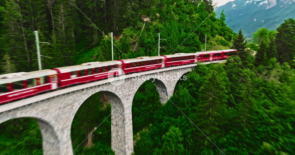Aerial video of the red train traversing the Landwasser viaduct. The Swiss Express travels through the green meadows and mountains of