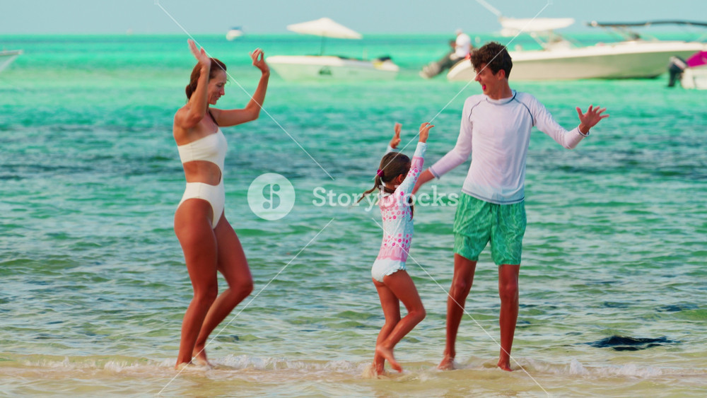 A mother with her children, a young daughter and a teenage son, dance in the crystal clear azure water of the Indian Ocean while having fun