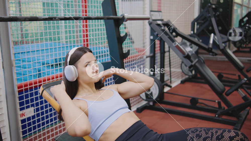 Fitness woman in headphones lifting weights in gym during workout session focusing on strength and fitness training