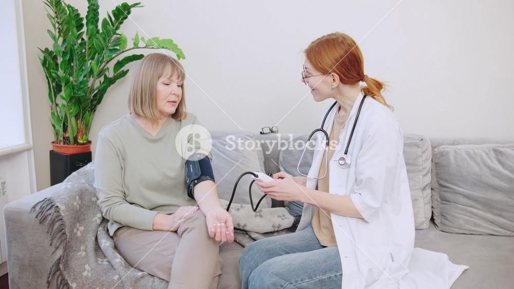 Red-haired house doctor. Medical worker checks blood pressure of elderly gray-haired patient in the comfort of his home during a routine