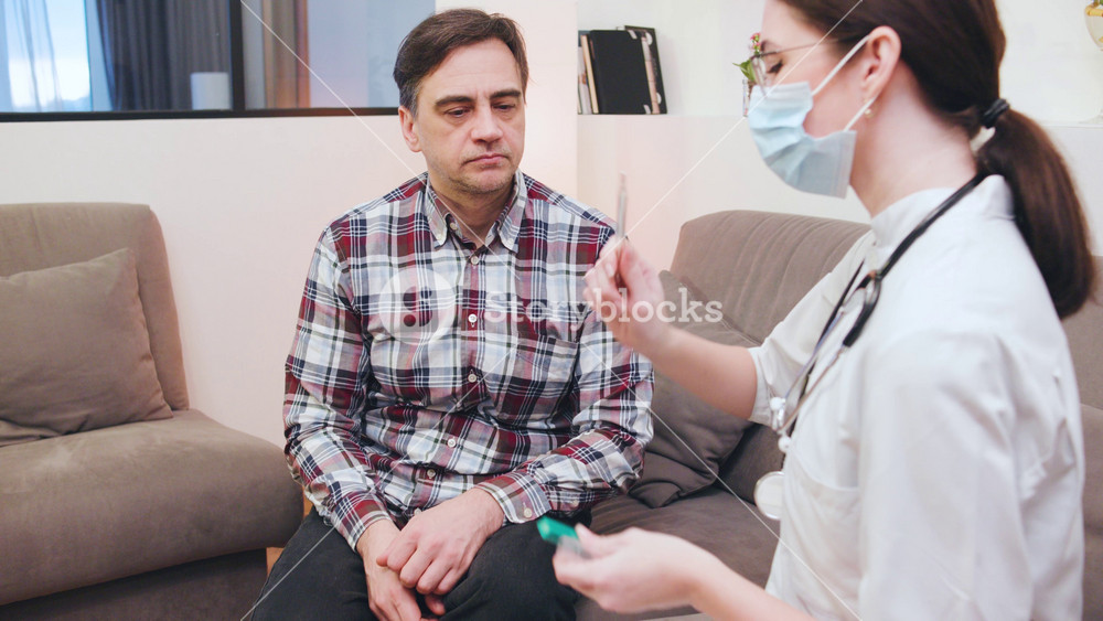 Doctor in medical mask consults with senior male patient giving him a thermometer to measure him temperature, discussing health concerns and