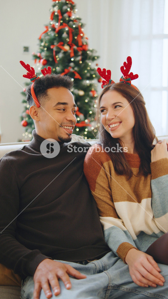 Portrait of happy multiracial couple celebrating Christmas and New Year together in front of a decorated Christmas tree at home,vertical