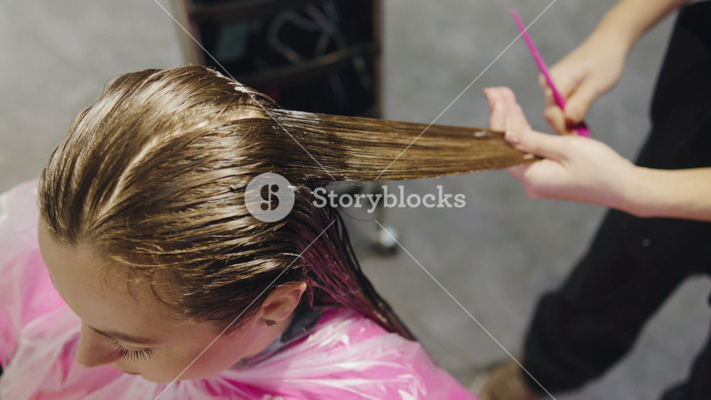 Styling hair with a comb and hair dye at a salon during the day with a focus on an adult woman getting her hair done