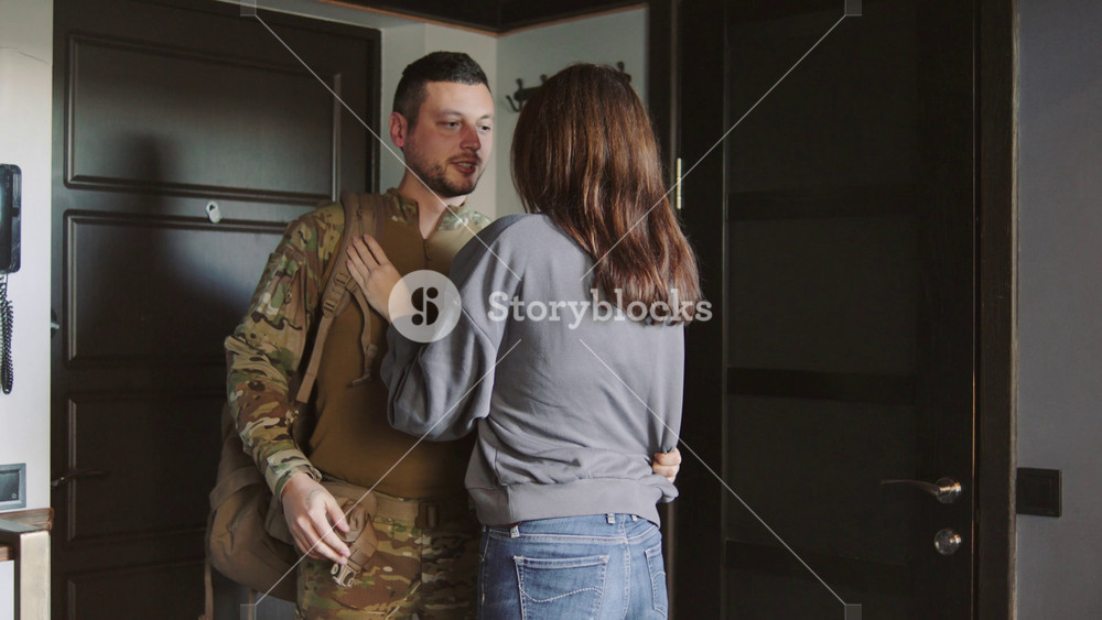A soldier leaves home for duty and hugs his wife goodbye in the hallway. She misses him and cries on the floor near the door.