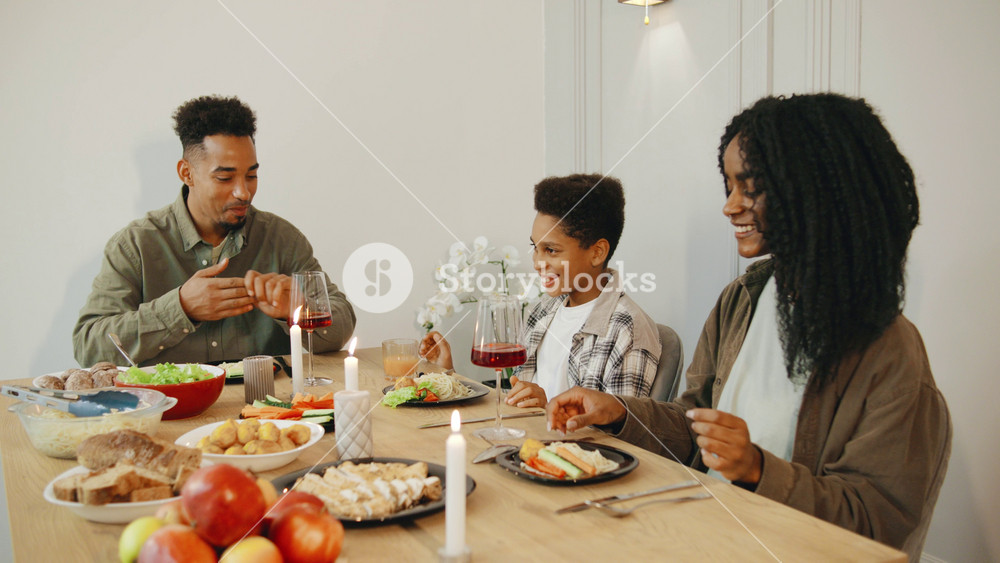 An African American family holds hands and closes their eyes as the father leads a heartfelt prayer of before their meal, sharing a moment