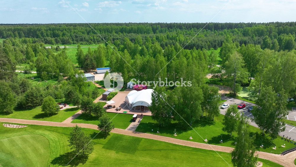 Dobrograd, Russia - May 12, 2024: An aerial drone view of a large white marquee tent set up for an outdoor event or party on a beautiful, green golf course