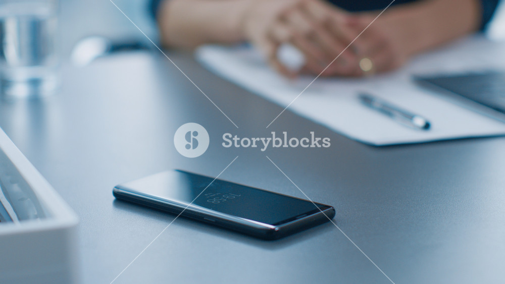 Businesswoman Working at Her Office Desk Reaches for Her Smartphone and Starts Typing Important Business Related Email. Woman Picks up Mobile Phone from Her Desk. Focus on a Phone